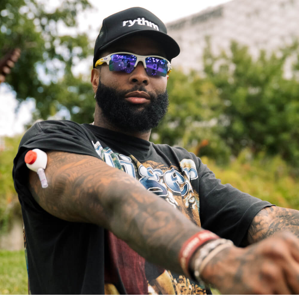 Man wearing a Rythm cap performs an at-home blood test using a small collection device on his upper arm, outdoors.