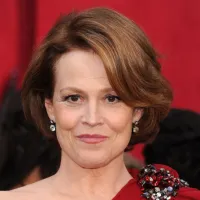 Sigourney Weaver wearing a red dress in front of a red background