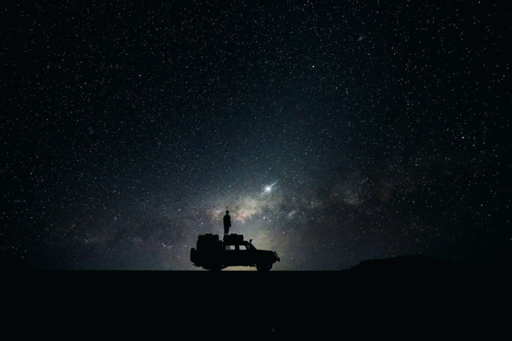 Silhouette of a person standing on the roof of a car under a starry night sky