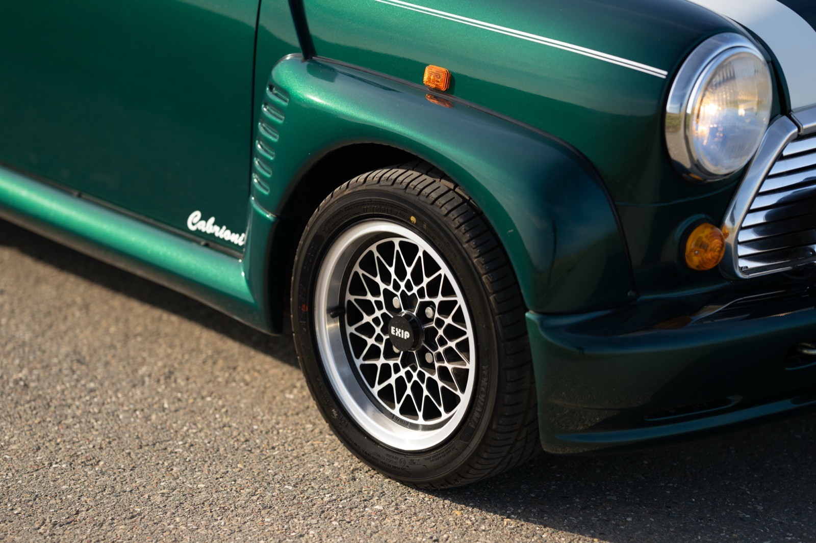 Close-up of a green vintage car's front wheel and tire, showcasing chrome accents and detailed tread.