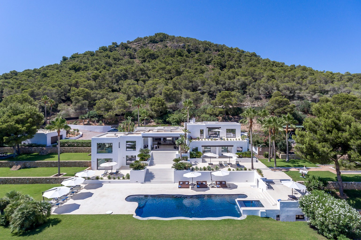 Modern Mediterranean luxury estate with infinity pool and panoramic hillside surroundings overlooking Ibiza coastline.