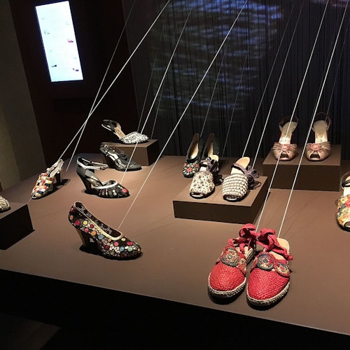 在灯光昏暗的房间内，各式设计师鞋款由细绳悬挂展示，并陈列于高台之上。