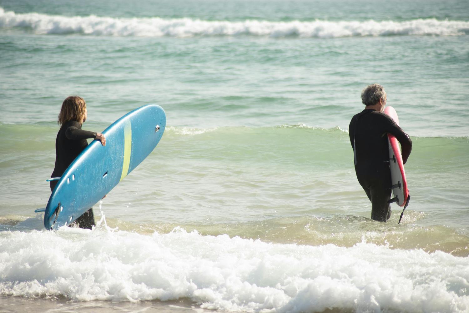 Two surfers walking along a sandy shoreline with their boards — surfboard rental in Middle East