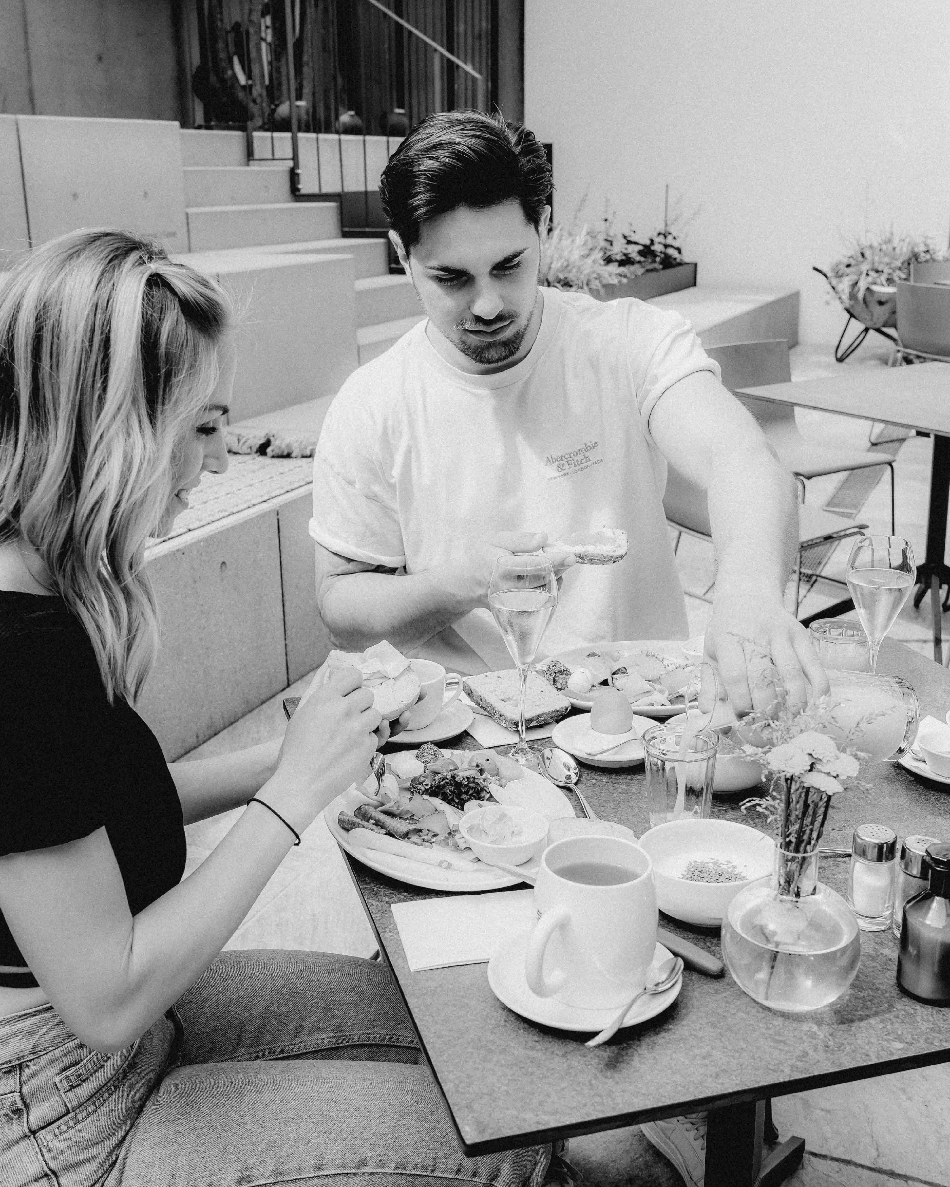 A man and a woman sit at a table enjoying a meal, surrounded by dishes and drinks, in a casual setting.