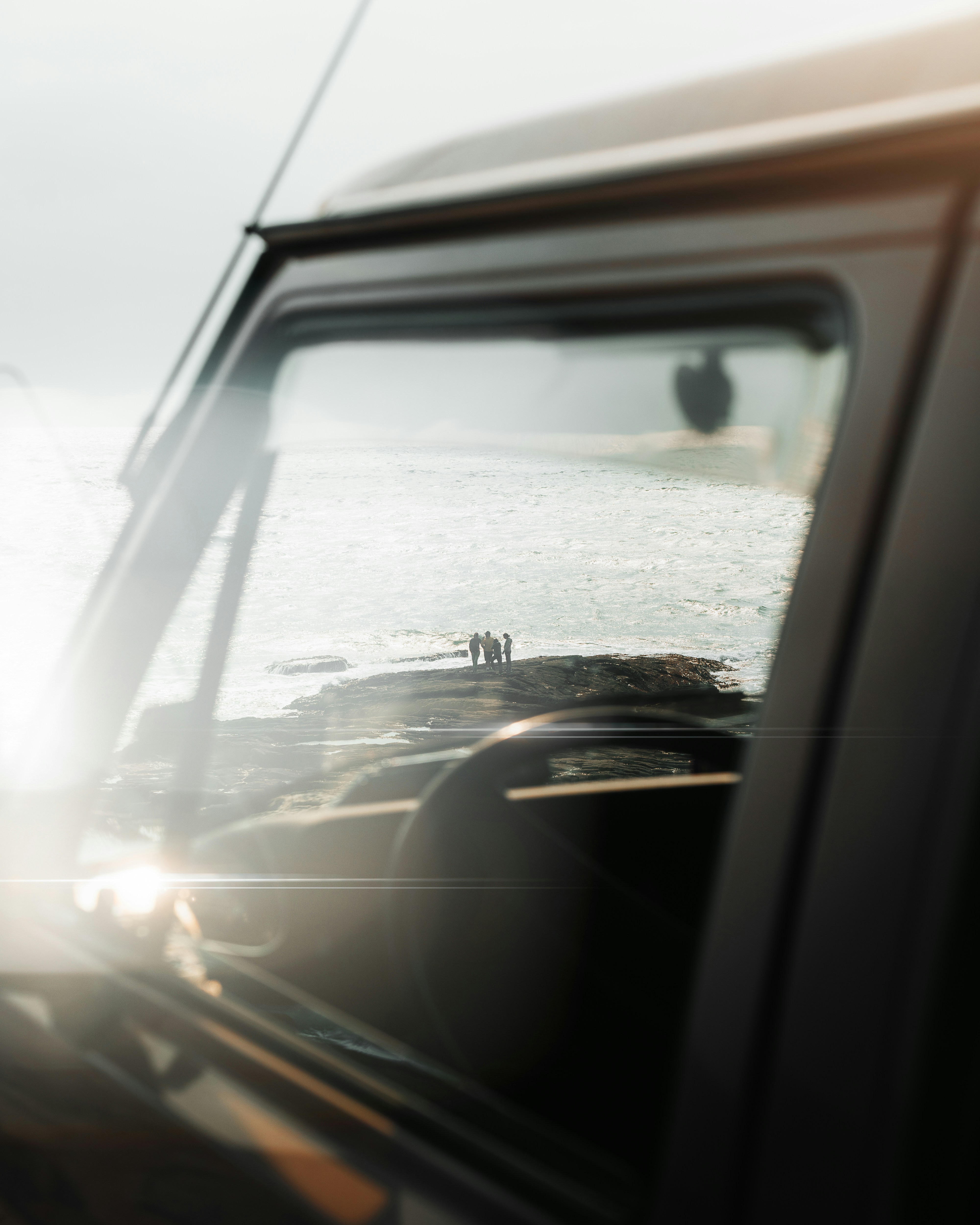 People reflected in car window by the ocean