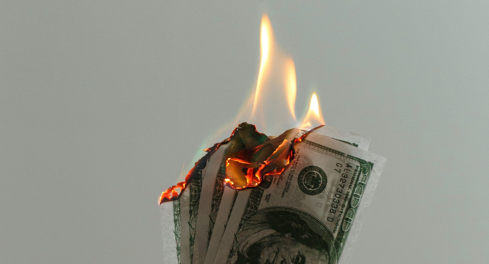 três cédulas de dólares com a ponta em chamas