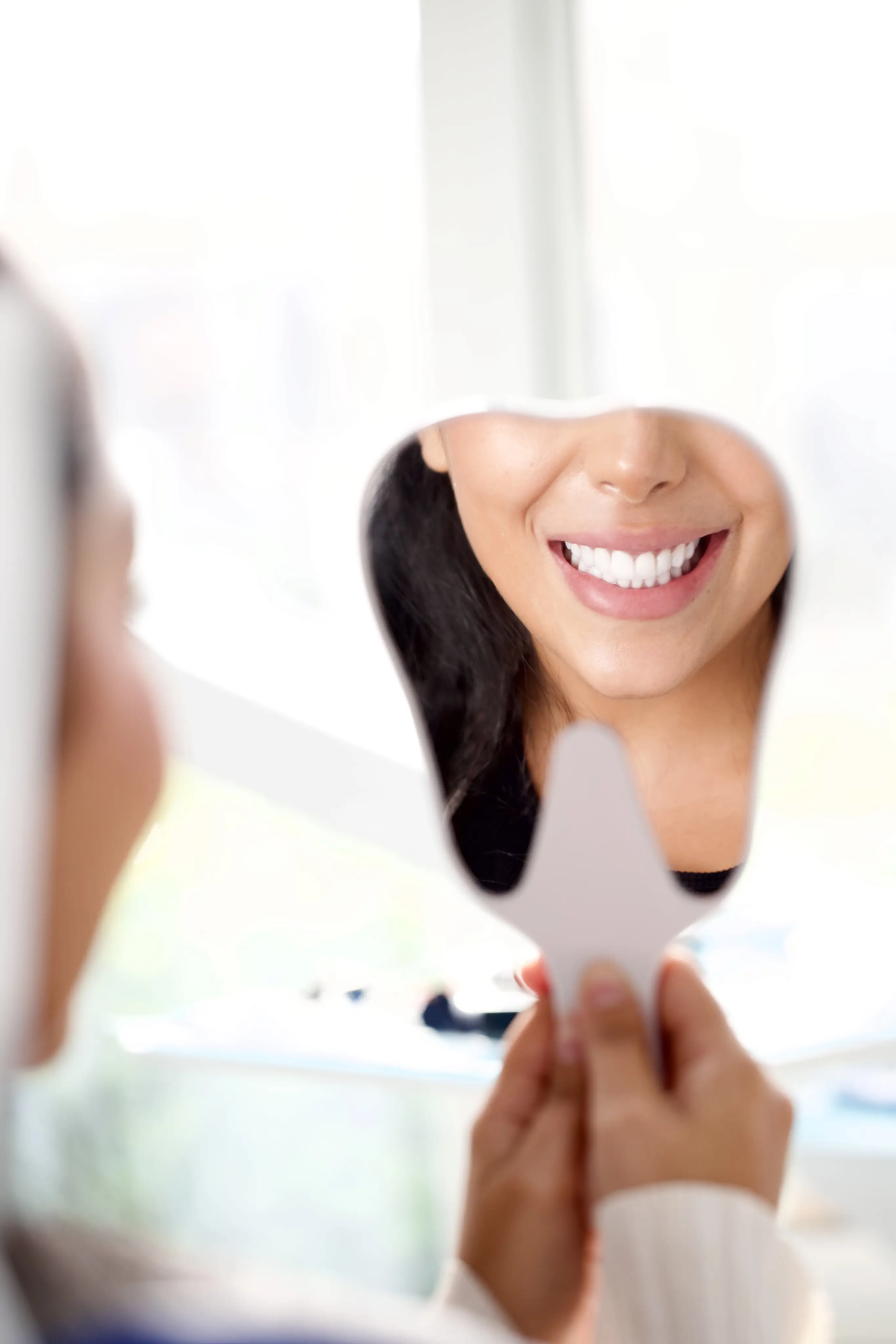 امرأة تبتسم في المرآة، تُظهر ابتسامتها الجميلة بعد نجاح عملية الفك في دبي.