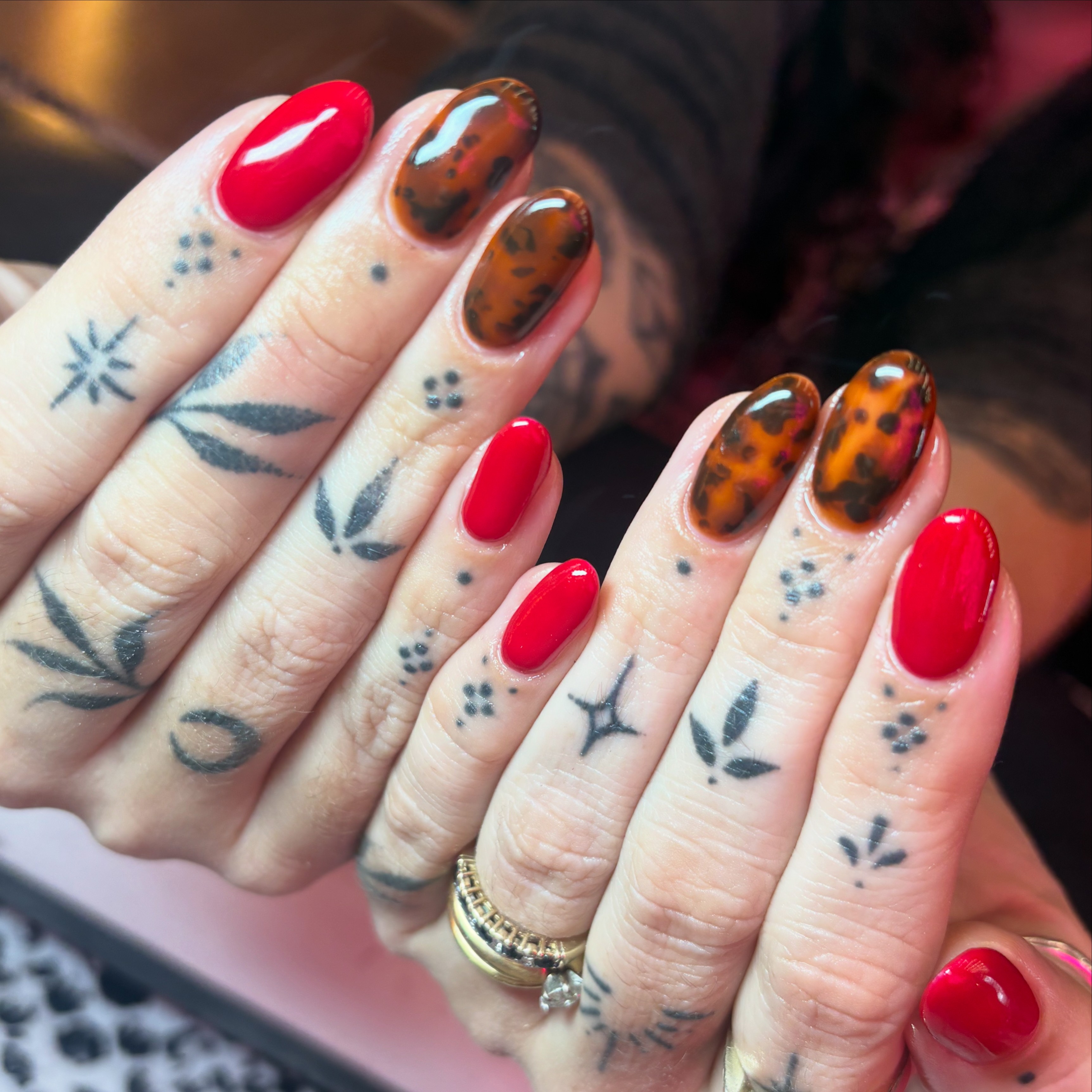 Short oval nails alternating between a solid glossy vibrant red and a realistic translucent amber tortoise-shell pattern.