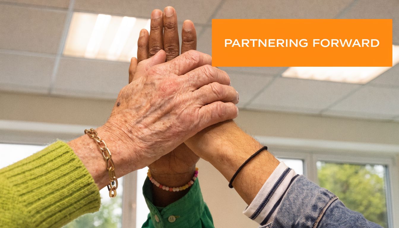 Multiple hands of diverse people stacked together in an office setting, symbolizing teamwork and collaboration.
