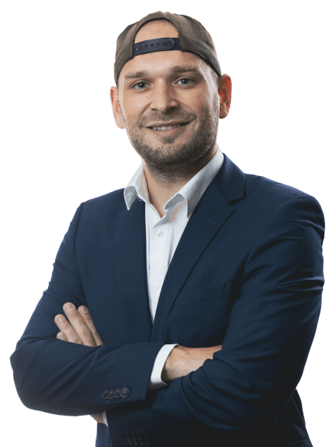 A smiling man in a suit and cap stands confidently with arms crossed against a blue background.