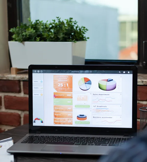Laptop on an office desk showing sales and performance charts on one dashboard