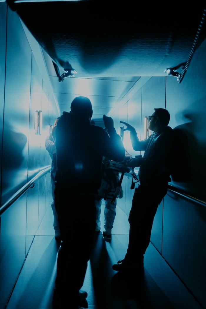 Person, holding a white rose behind his back with one arm on a light blue background