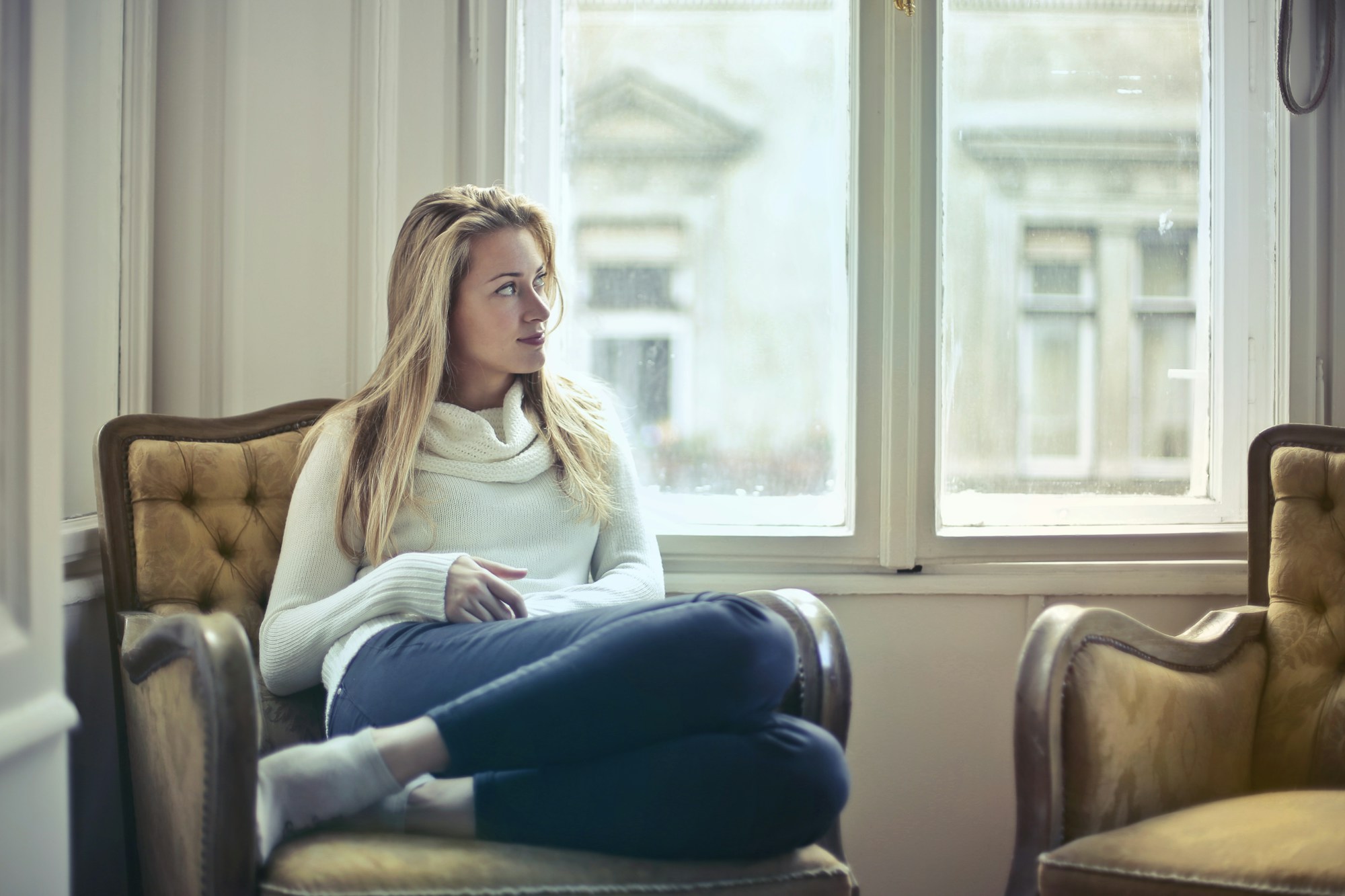 Woman sitting in an armchair by a window, thinking