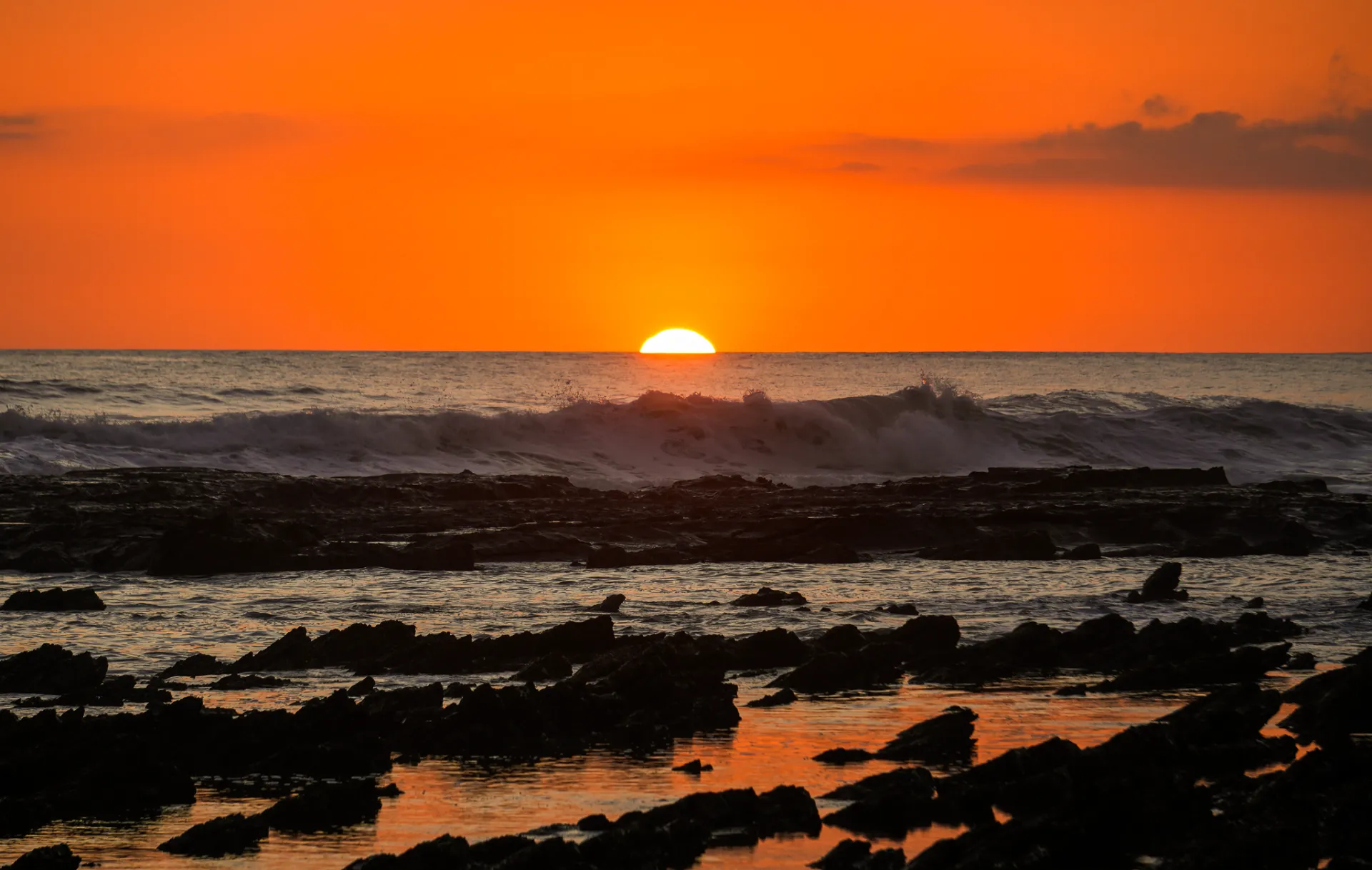 Orange sunset over the Pacific with waves breaking on rocky tide pools