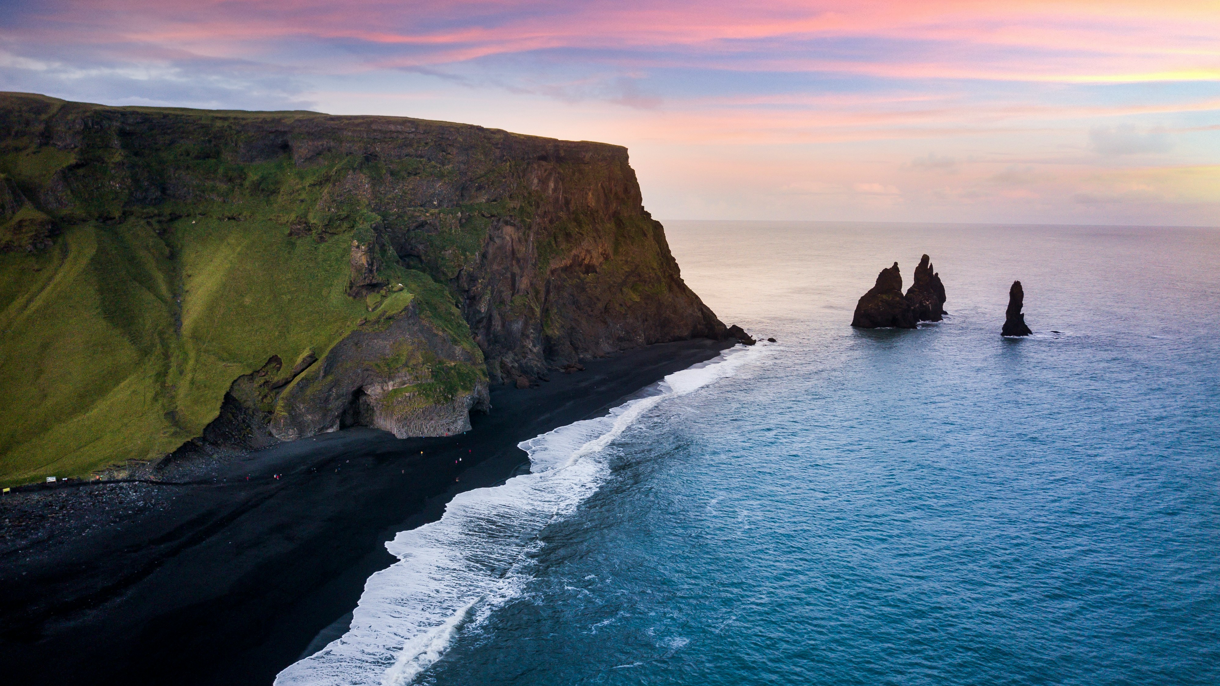 Soft pink sky over Reynisfjara black sand beach and the Reynisdrangar sea stacks in South Iceland.