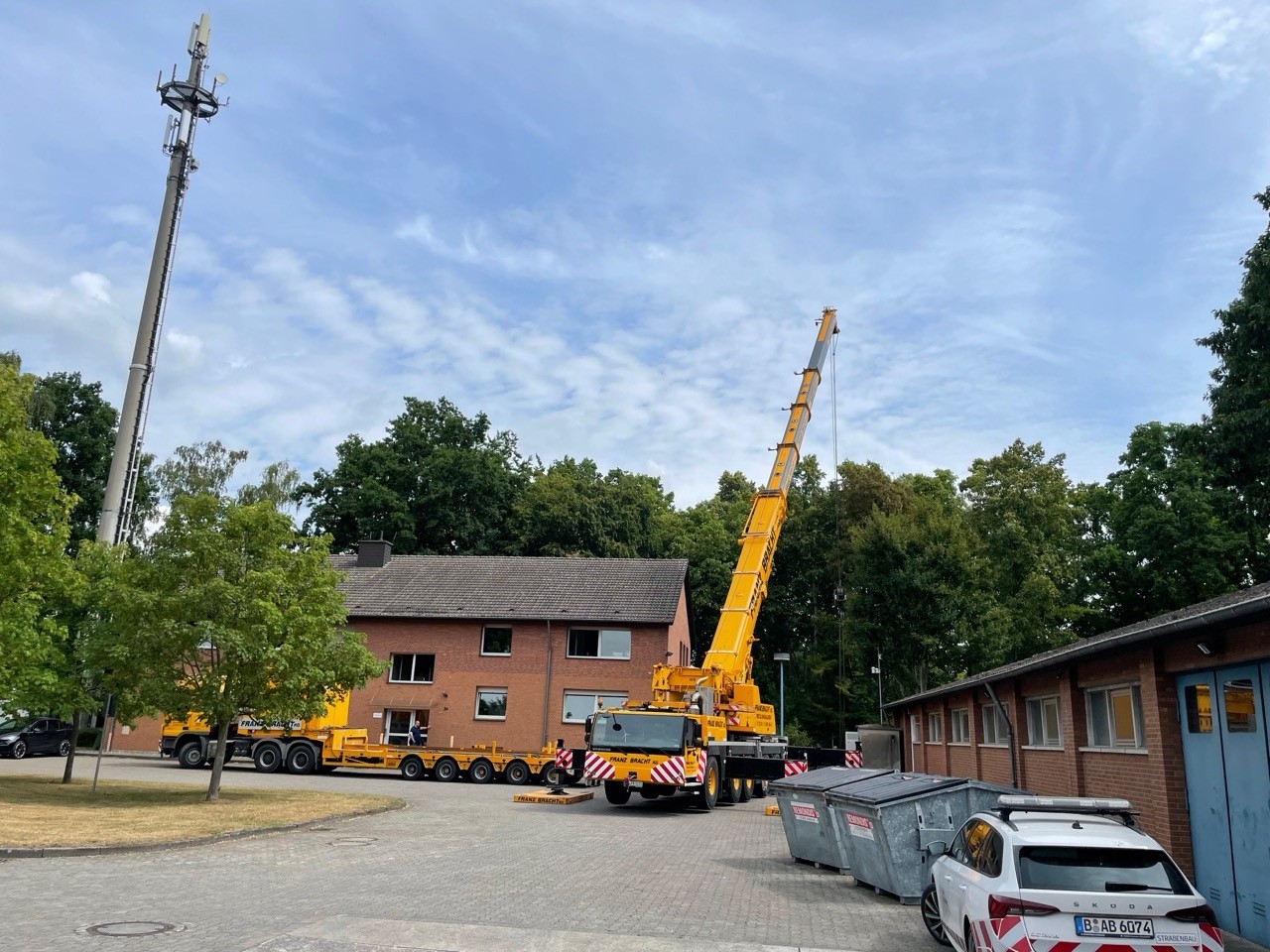 Schwerlastkran hebt Objekt, Bauarbeiten neben Gebäude. Gelber Kran, Transport von Schwergut. 