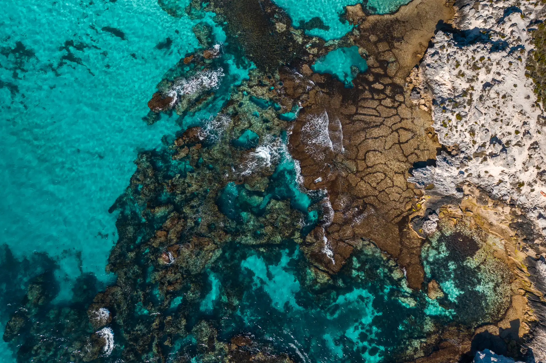 Aerial looking down on reef and rock ledges under clear turquoise water