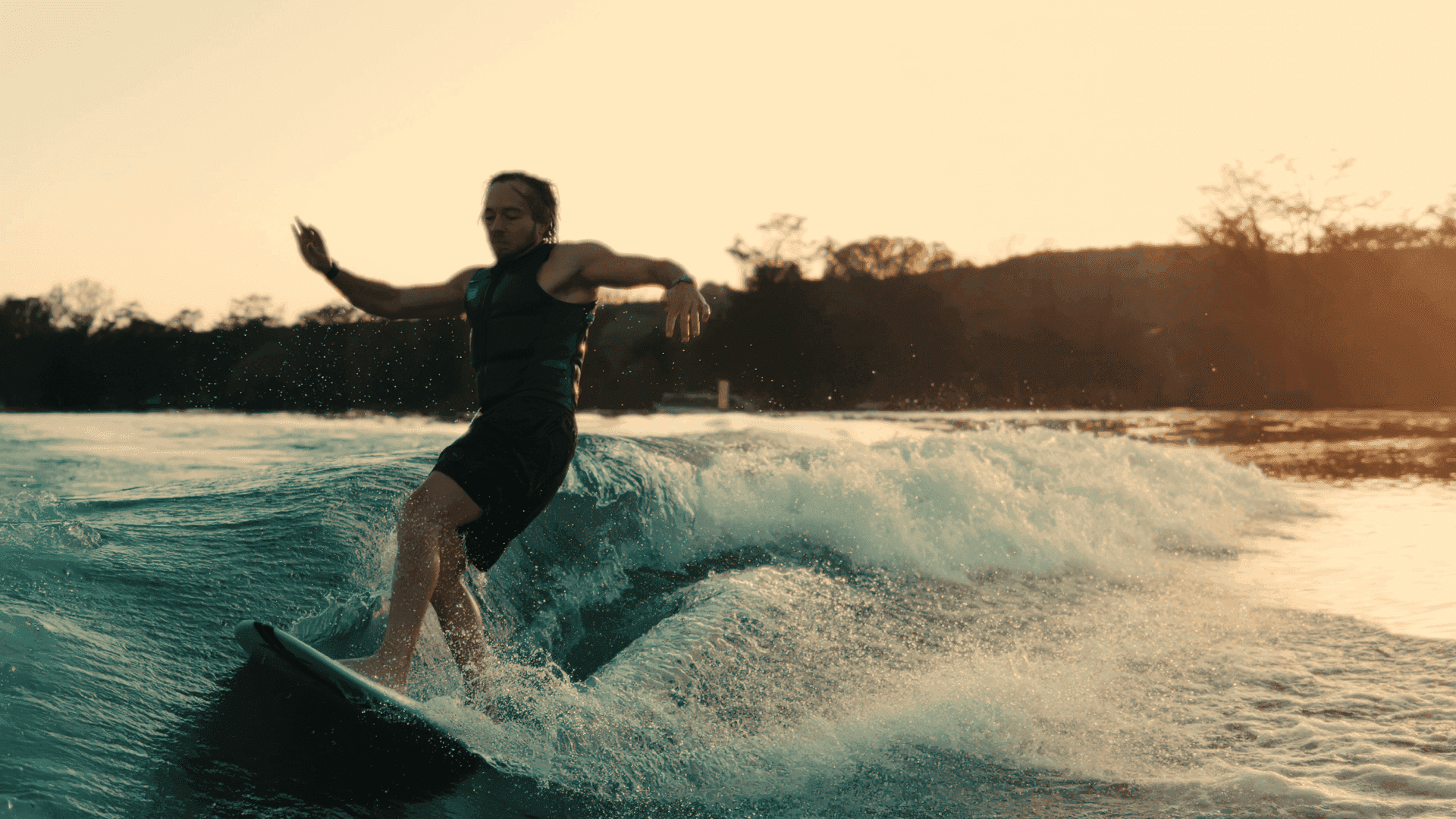 A surfer skillfully rides a blue ocean wave at sunset, with a silhouette of distant hills under a golden sky, epitomizing the thrill of surfing and adventure sports.