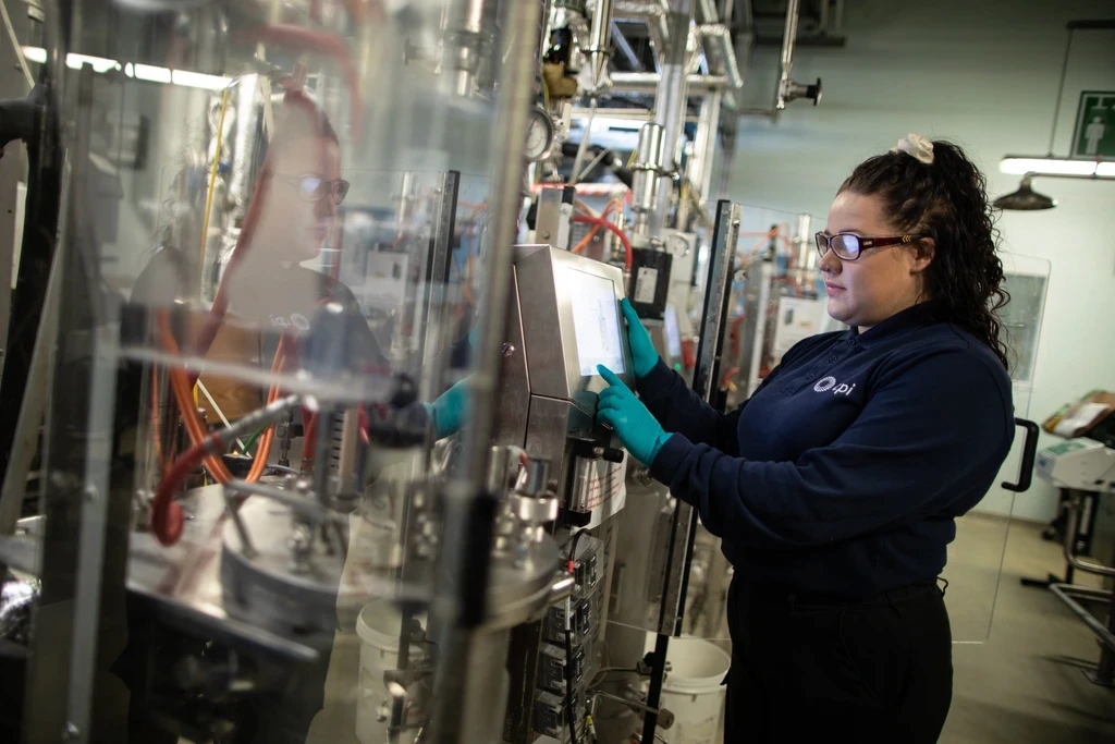 CPI scientist using a touchscreen control panel on a bioreactor system behind a glass screen.