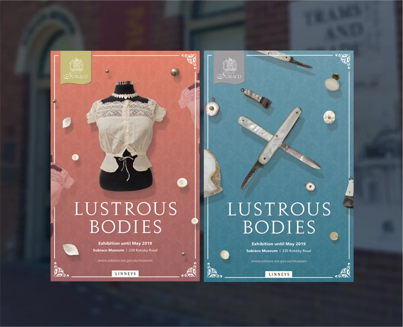 Two vertical exhibition posters for "Lustrous Bodies" at the Subiaco Museum. The left poster is a muted rose color featuring a white lace garment on a mannequin, while the right poster is a slate blue featuring an arrangement of vintage pearl-handled pocket knives and buttons. Both posters include the City of Subiaco and Linneys logos.