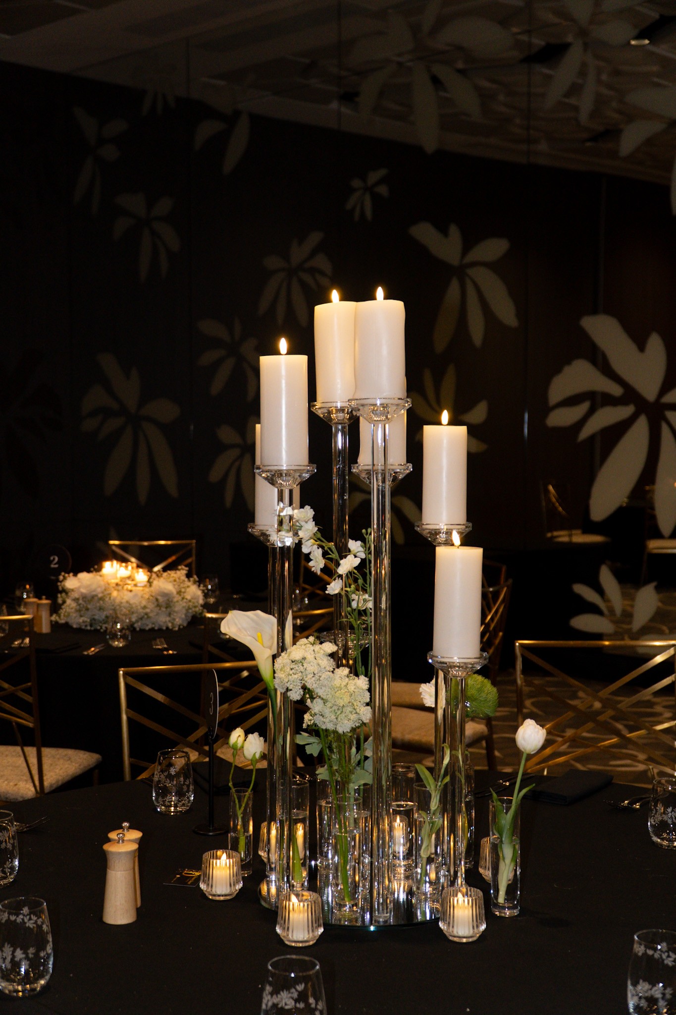 White candles in tall glass holders lighting a wedding reception table.
