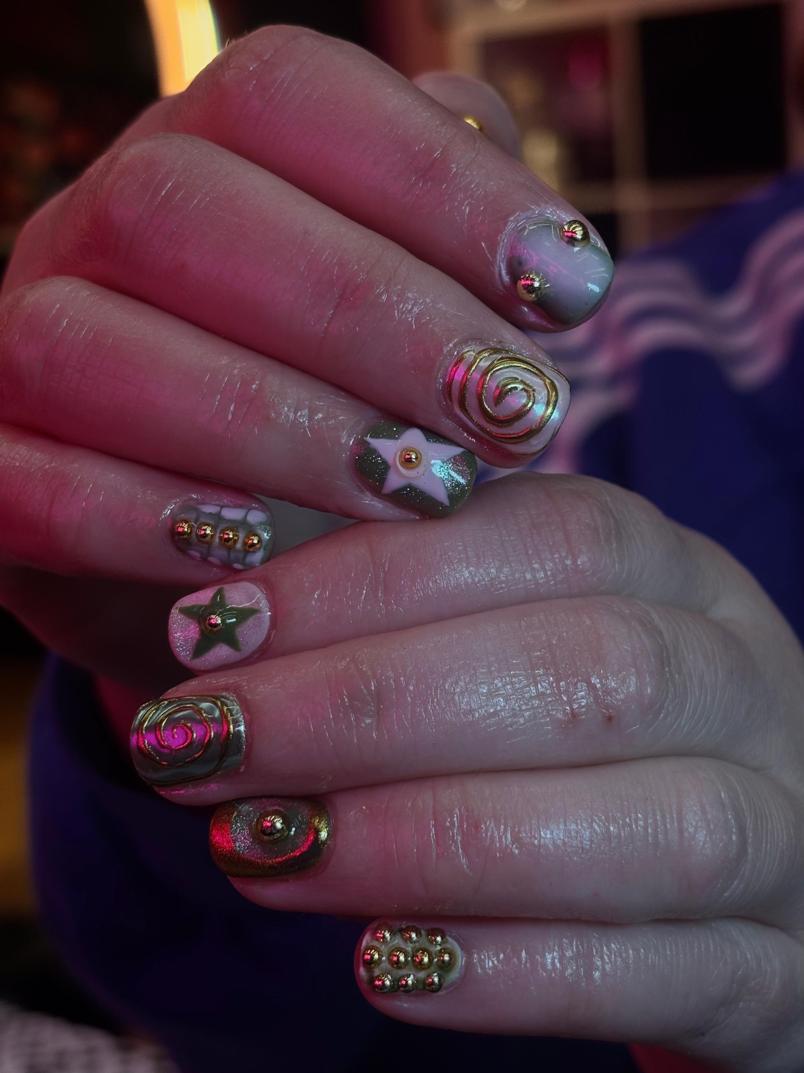 Short natural nails with a sage green and dusty rose palette, heavily decorated with 3D gold chrome swirls, gold caviar beads, and star charms.