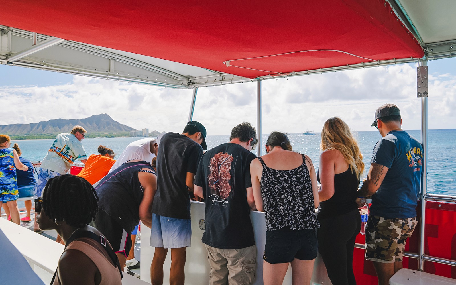 ผู้เข้าชมที่กำลังชมชีวิตใต้ท้องทะเลบนเรือท้องกระจกในฮาวาย โดยมีภูเขาไฟ Diamond Head เป็นฉากหลัง