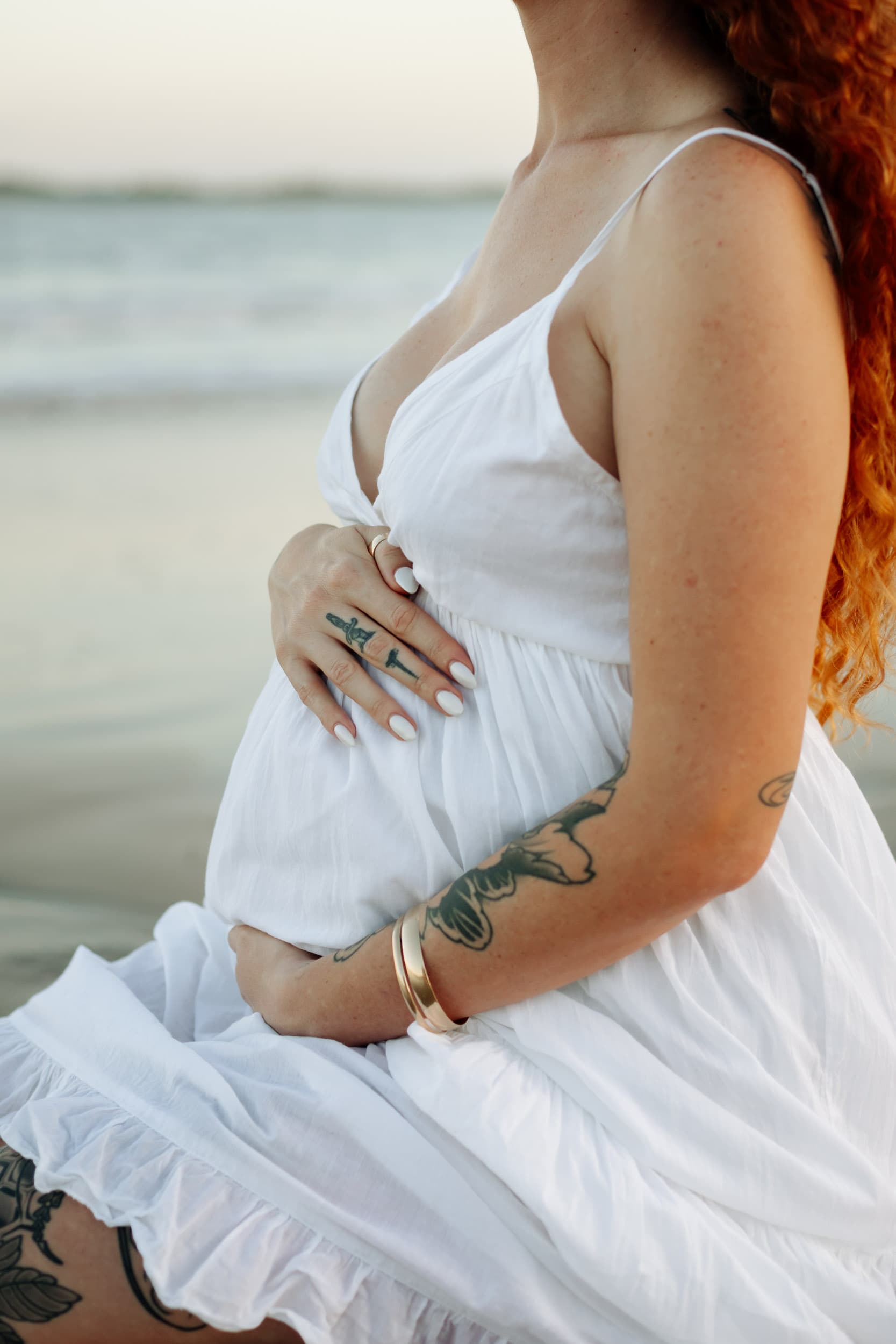 Close-up maternity image of pregnant mother holding her belly with warm sunset light reflecting off the ocean behind her.