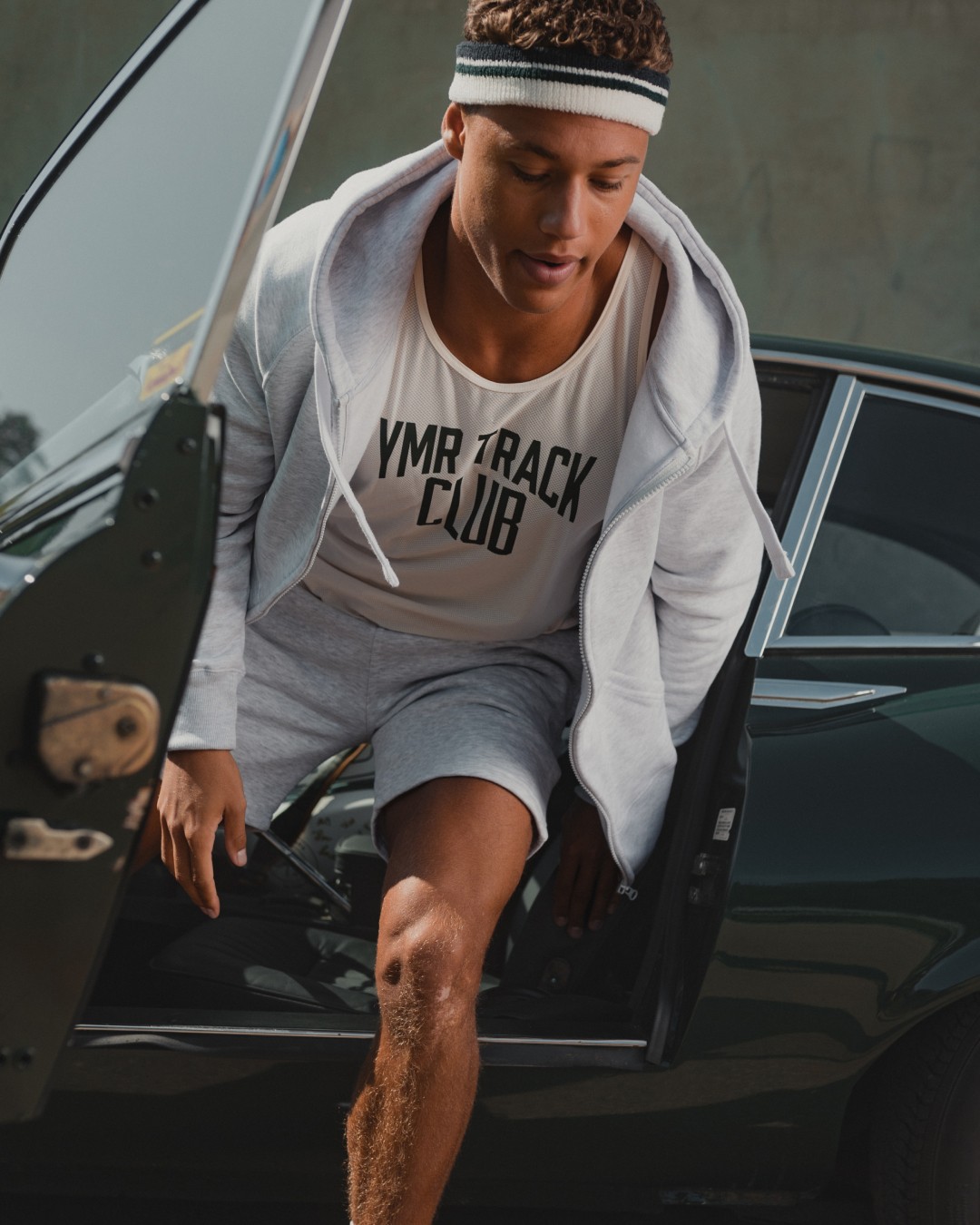 Person wearing shorts and ziphoodie stepping out of green car