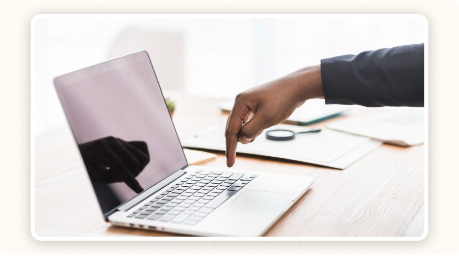 Hand pointing at laptop screen on desk