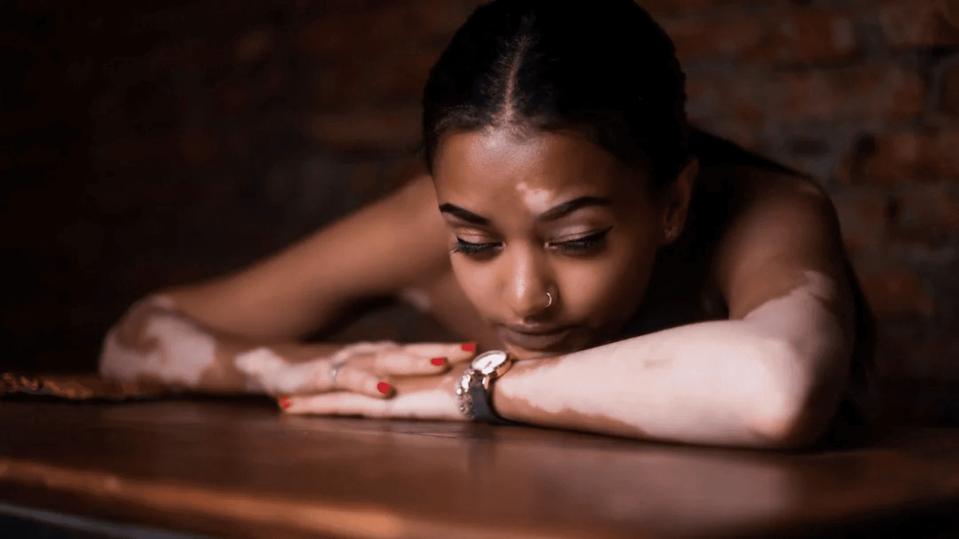 a young girl with dark hair rests her chin on her folded arms on top of a wooden desk