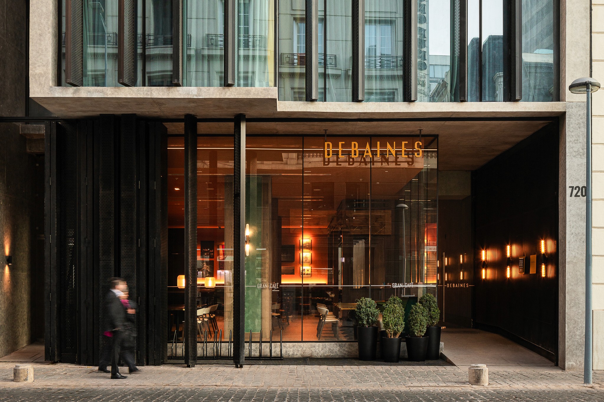Modern building entrance with large glass windows, featuring warm lighting and a small plant by the door.