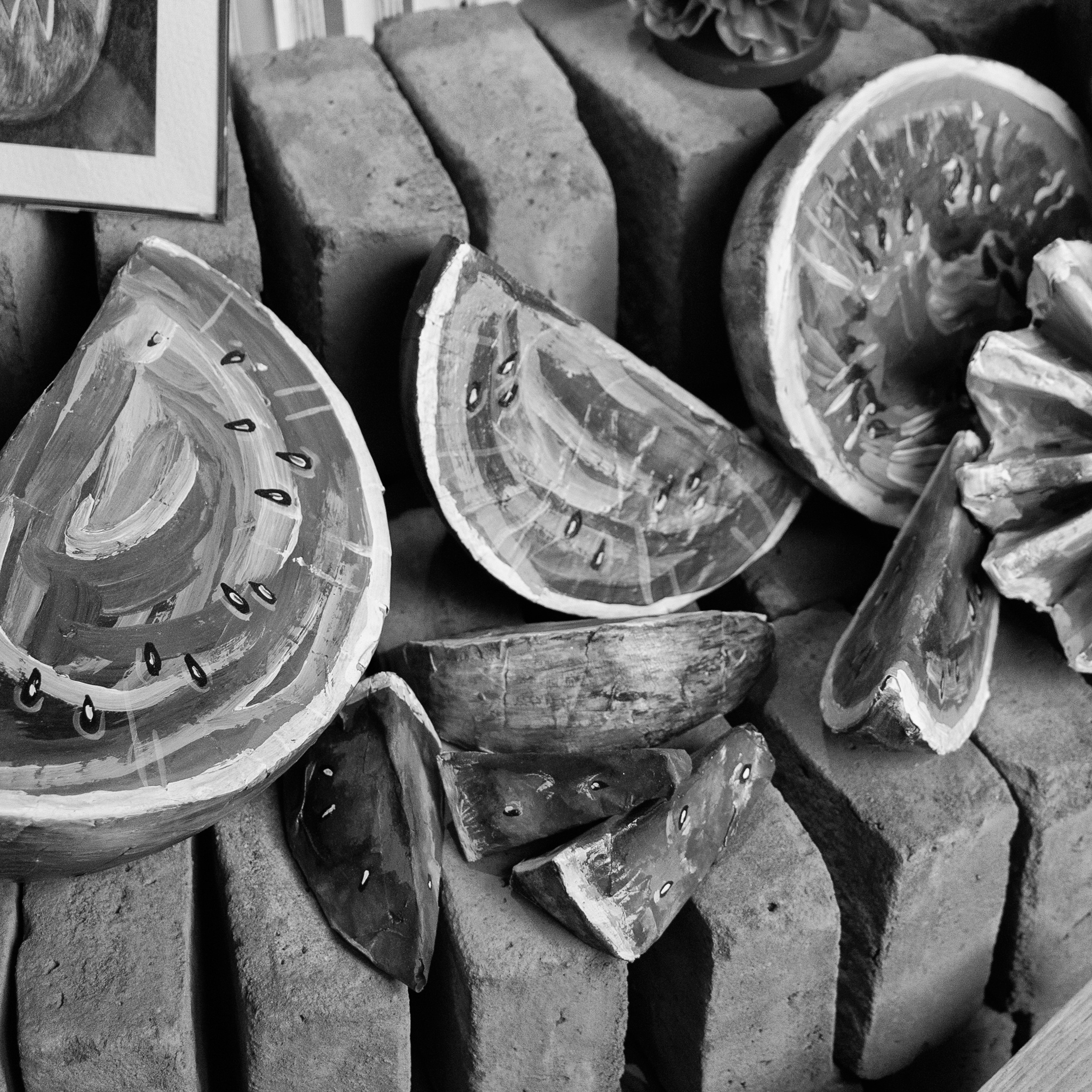 Black and white photograph of hand-painted papier-mâché watermelon slices arranged on stacked bricks, capturing a festive, artisanal feel.