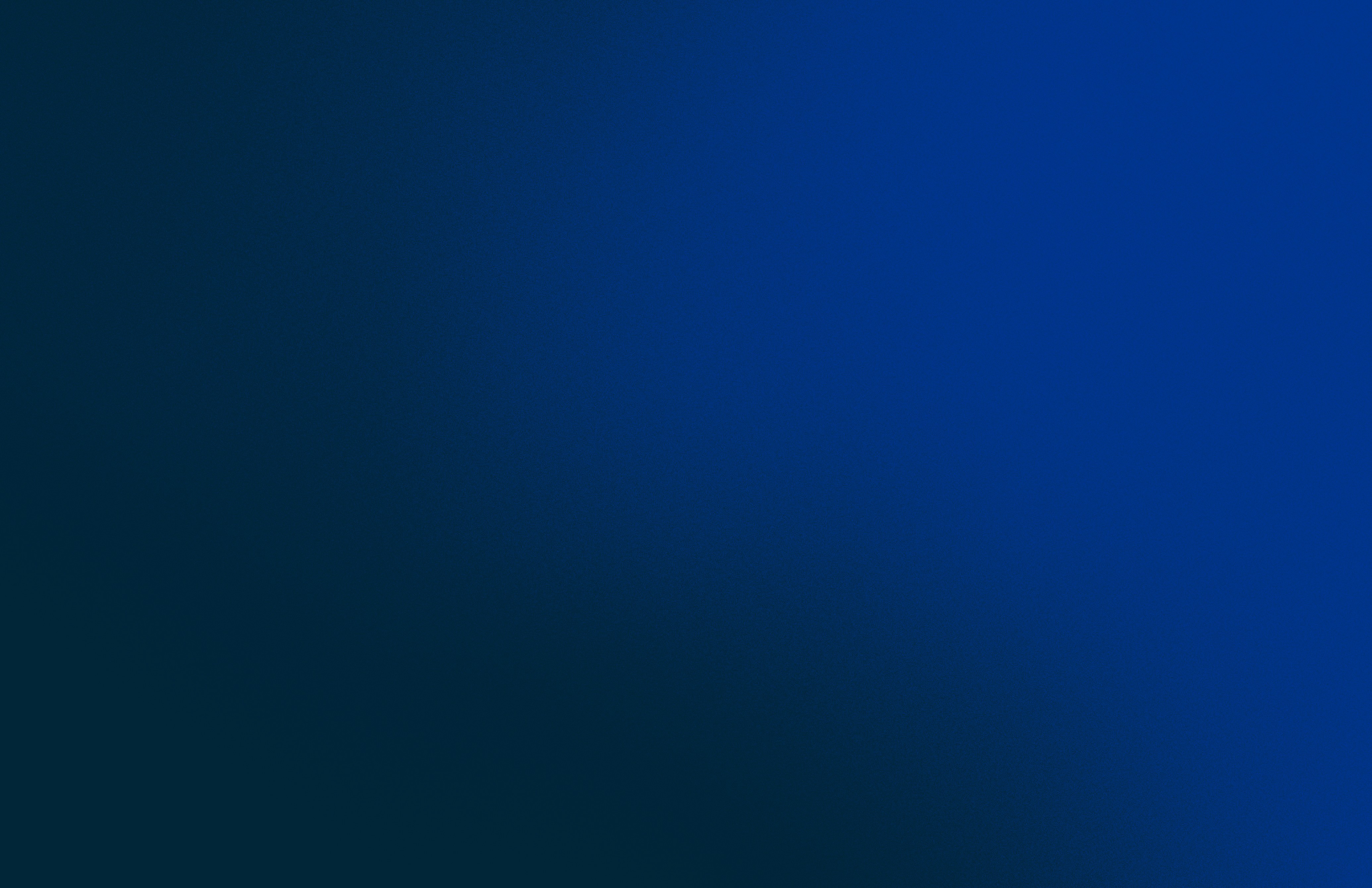 A man stands while two people sit at a table in an office setting, smiling and engaged in conversation. The mood is friendly and collaborative.