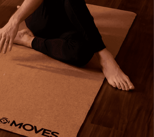 Diverse group practices yoga on cork yoga mats in a warm studio: warrior, tree, and seated poses.