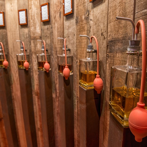 Üvegedények sora narancssárga izzókkal, mindegyik borostyán színű folyadékkal töltve, rusztikus fa falpanelekre szerelve.