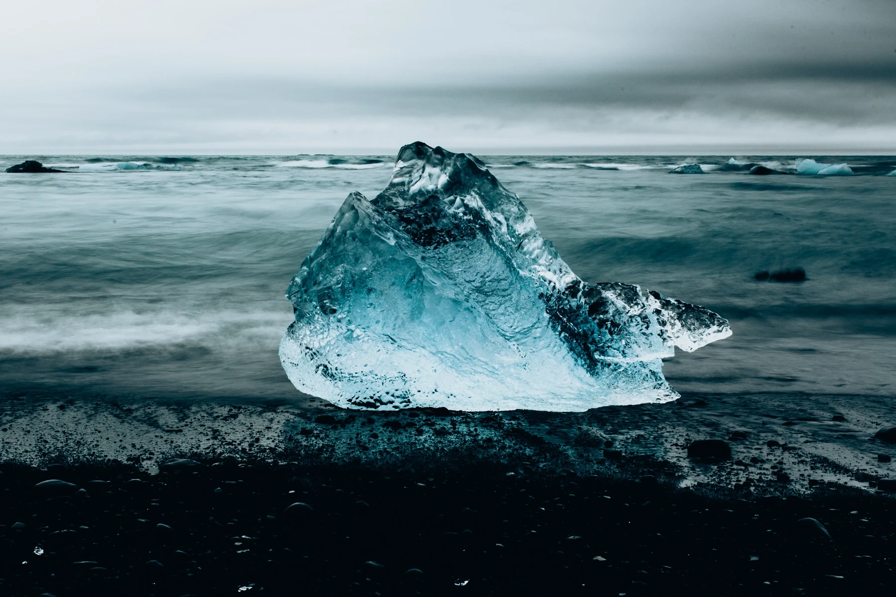 A jagged iceberg on a black sand beach, waves streaking past in long exposure