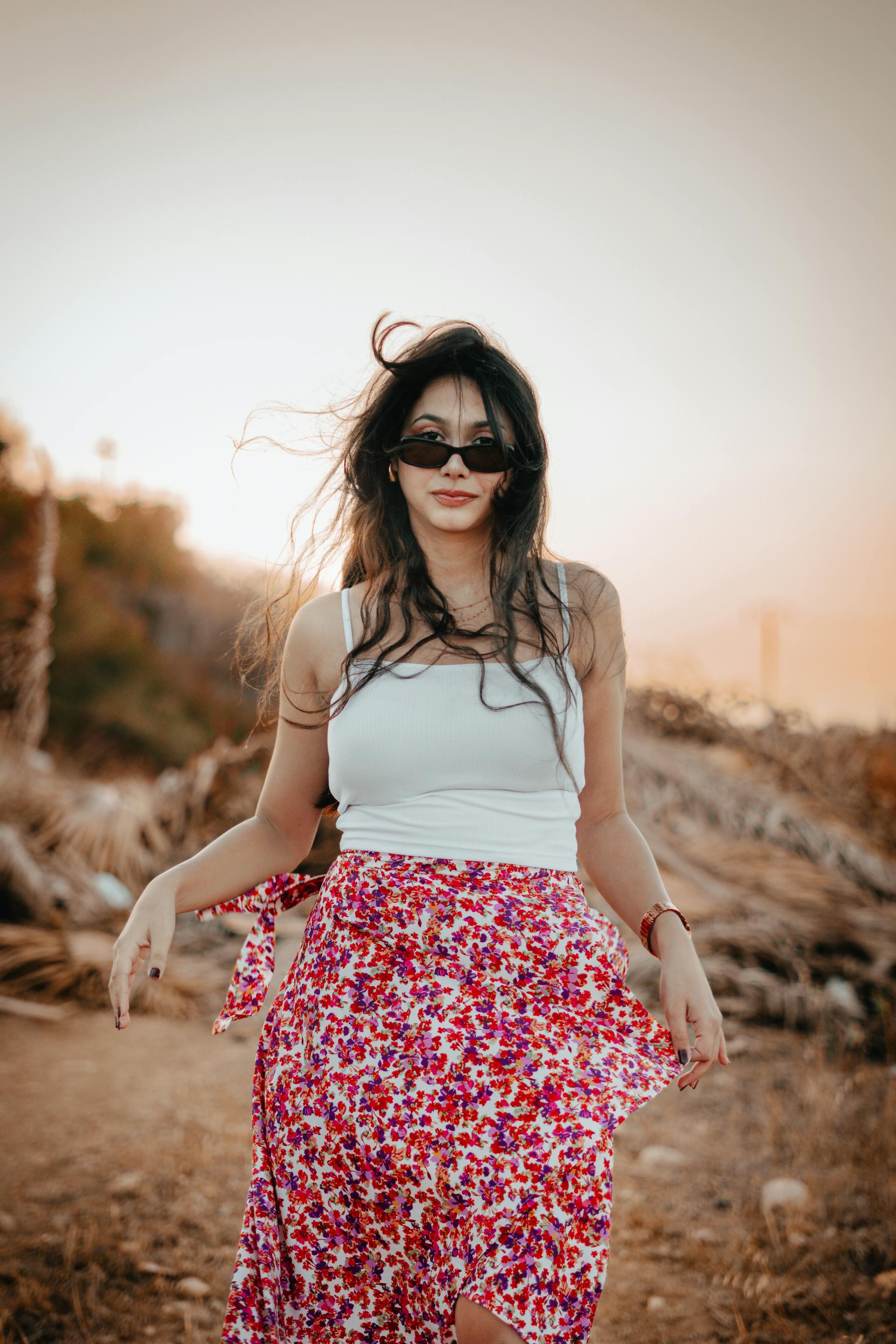 A woman wearing a floral skirt and a white top stands gracefully, showcasing her stylish outfit against a neutral background