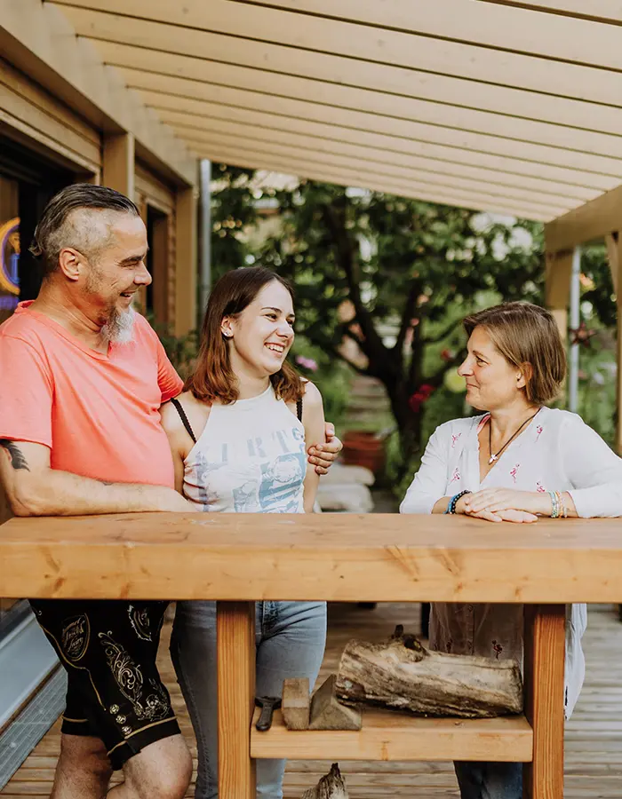 A man and a woman, along with their teenage daughter, are standing on a terrace, smiling at each other.
