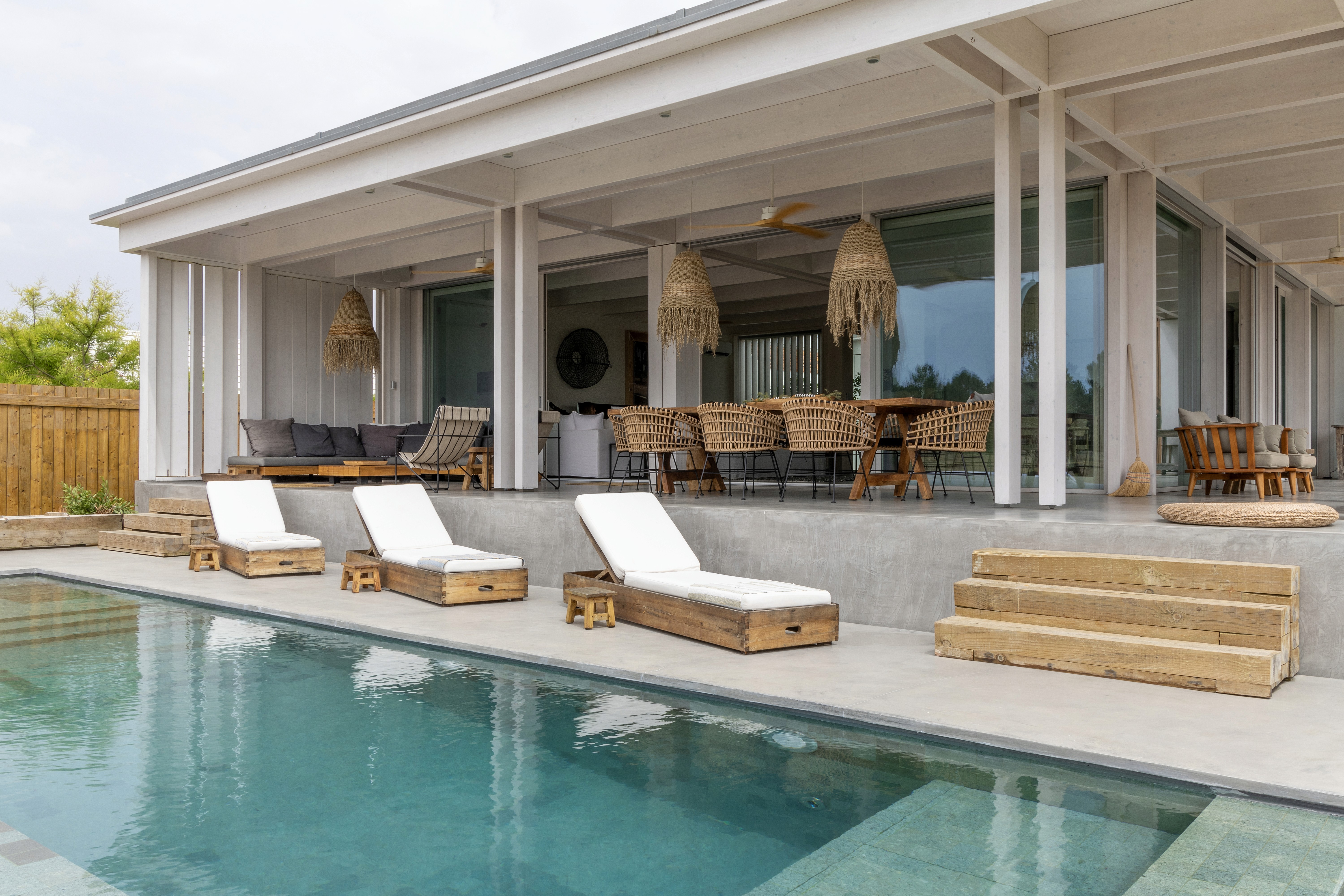 Cozy reading nook with sofa, chair, and plants inside a glass cabin with mountain forest views.