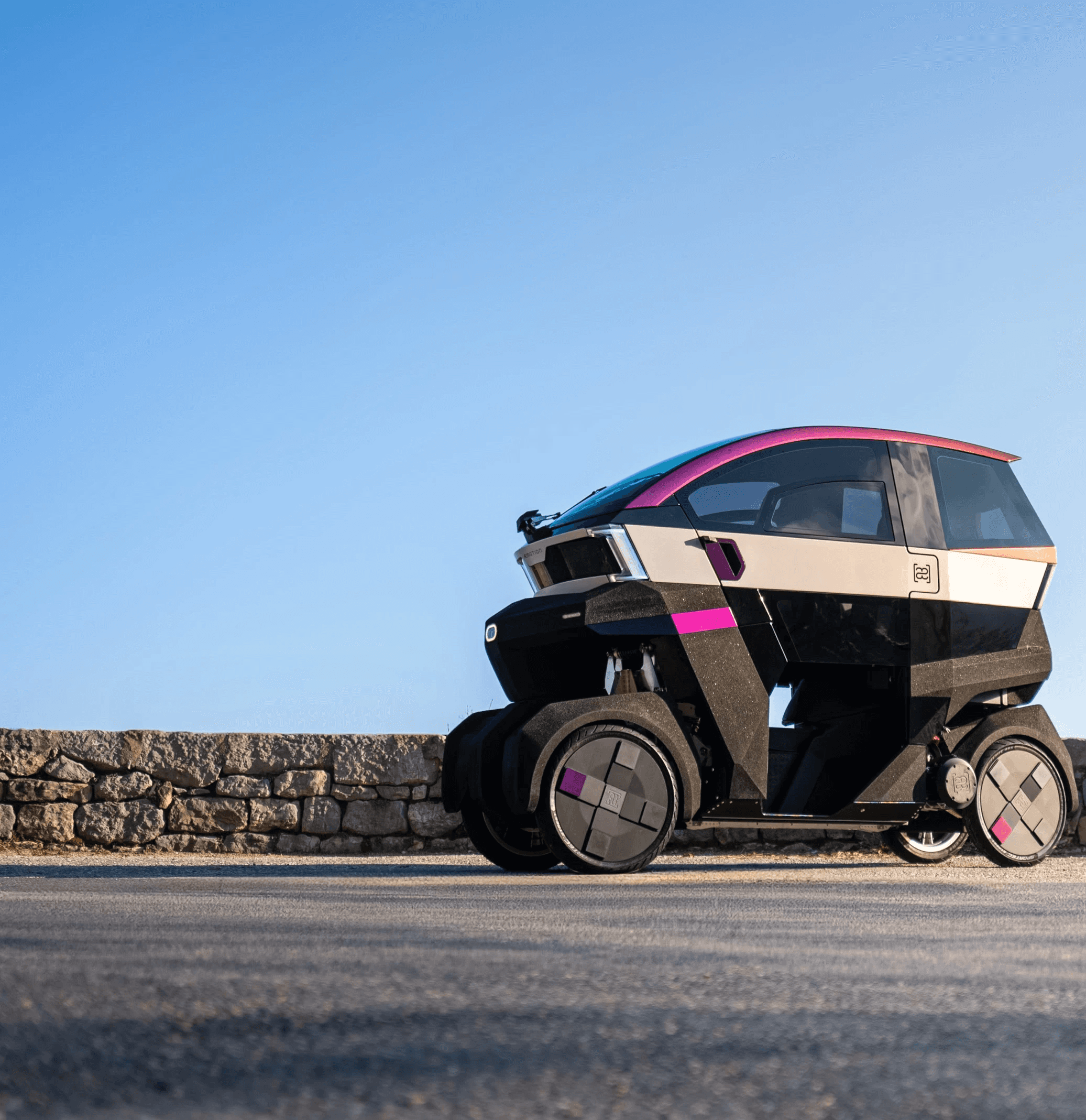 Futuristic enclosed three-wheeled electric vehicle parked on a quiet road under a clear blue sky.