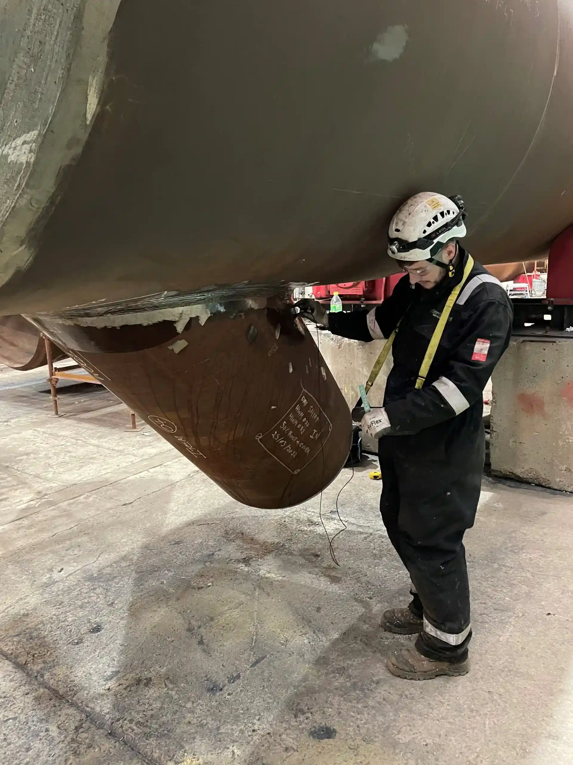 A worker in protective gear and helmet inspects a large industrial pipe inside a facility. The environment is industrial, emphasising safety and focus.