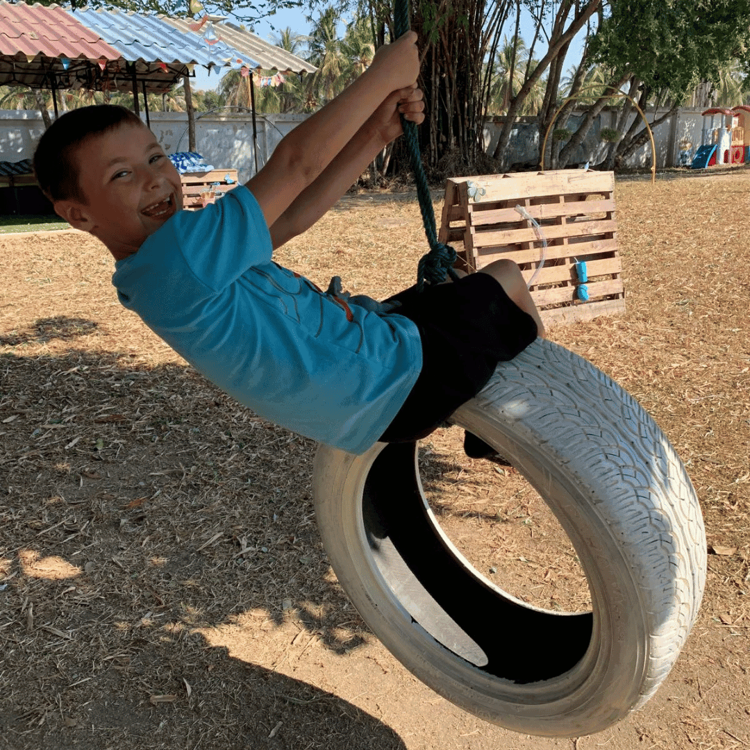 A young boy on a tire swing smiling towards the camera