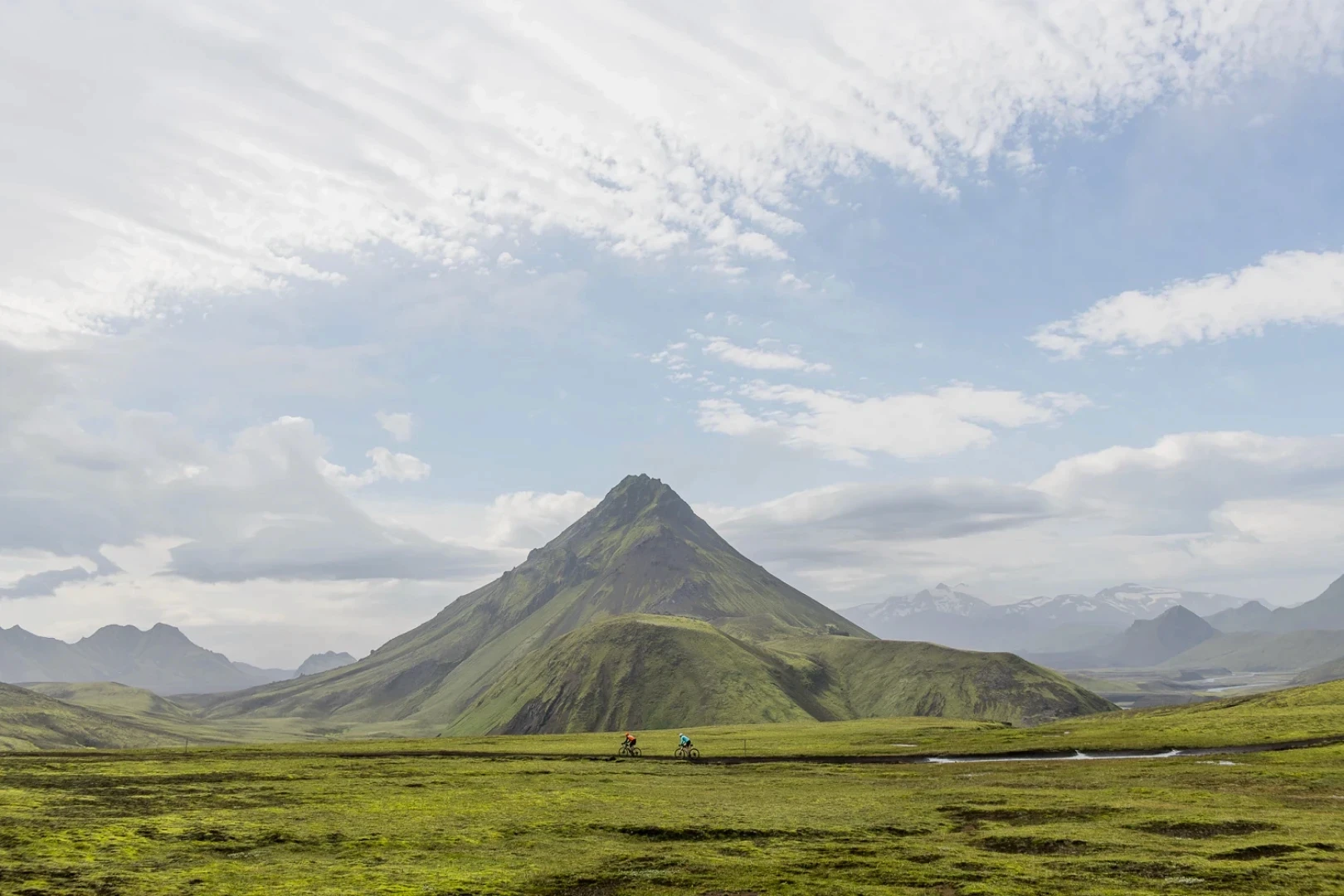 Wide green mountain landscape with gravel riders in Iceland highlands