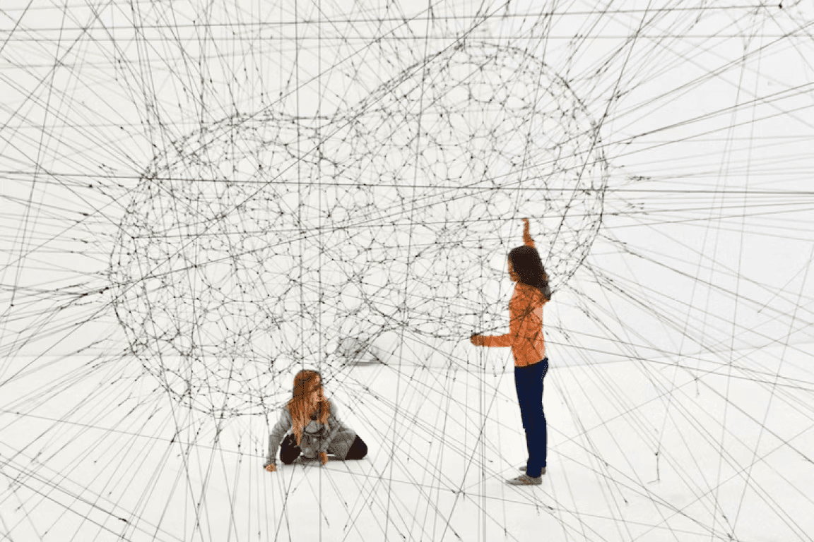 two women building a large art installation using string and cables - meant to represent machine learning
