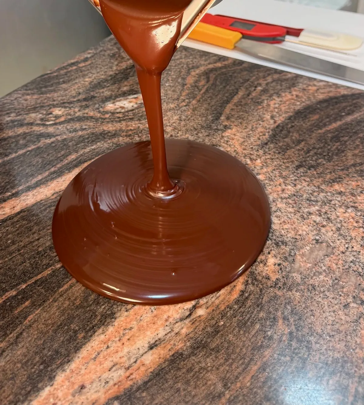 Molten chocolate is poured onto a surface during a tempering demonstration. 