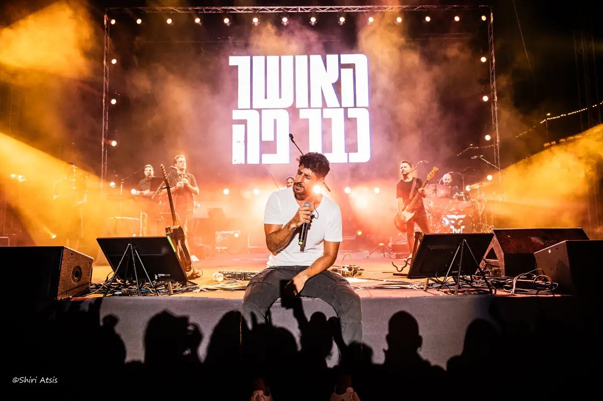 עידן עמדי יושב על שפת הבמה ברגע אינטימי עם הקהל, צילום הופעות של שירי עציץ - סטודיו Shiriz.