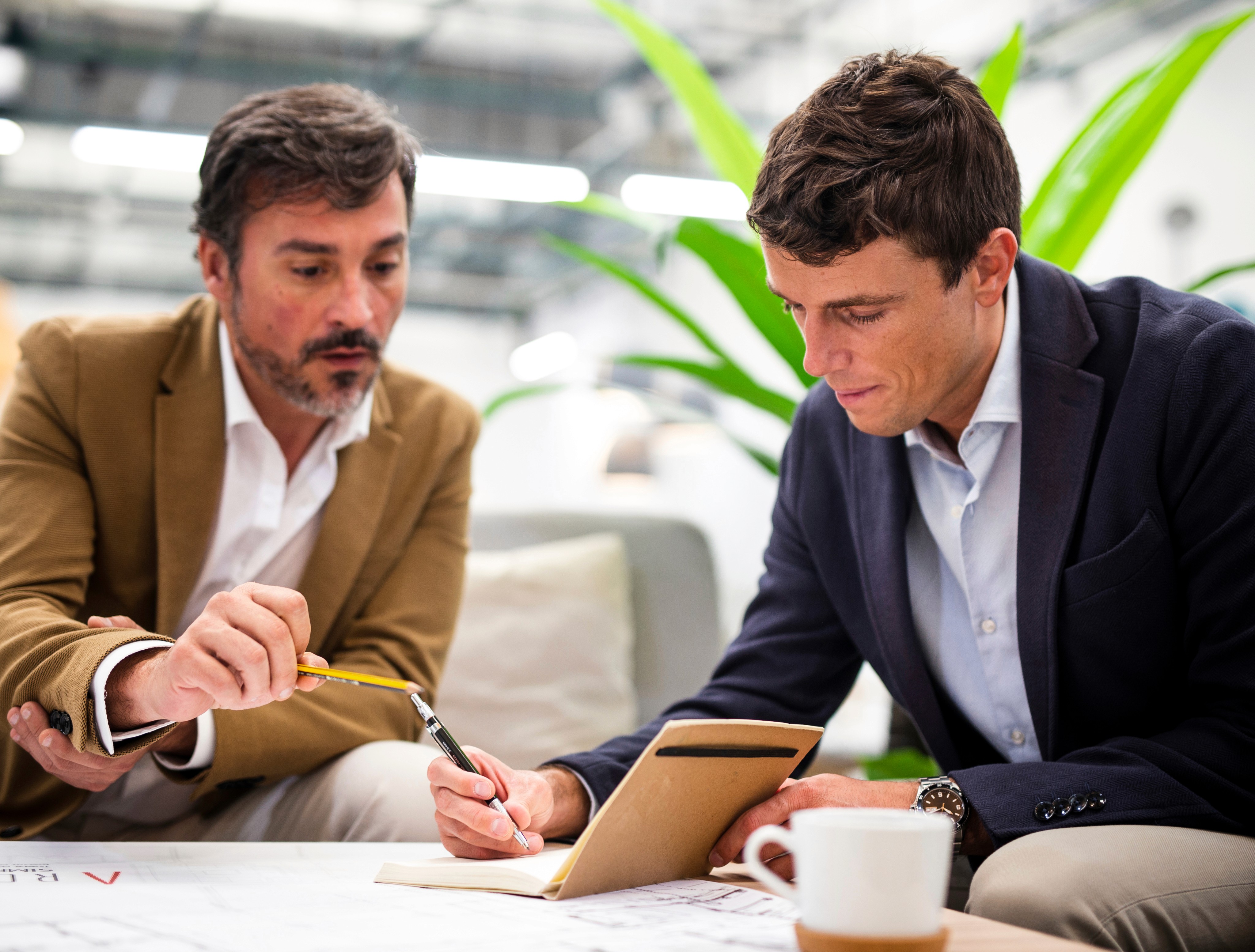 Two professional businessmen discussing and writing notes in a modern office.