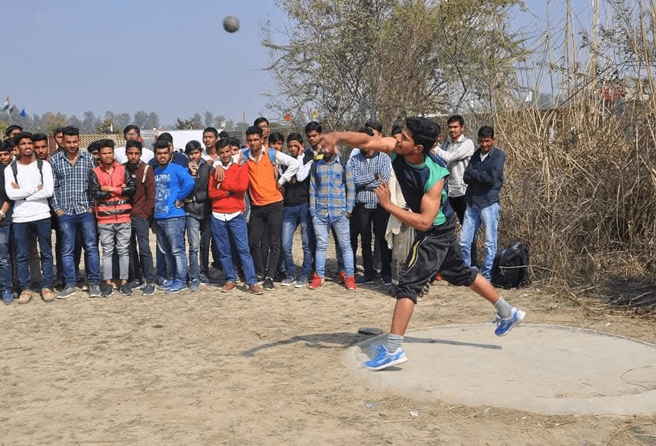 A male college student competing in a shot put event during a sports meet while classmates watch.