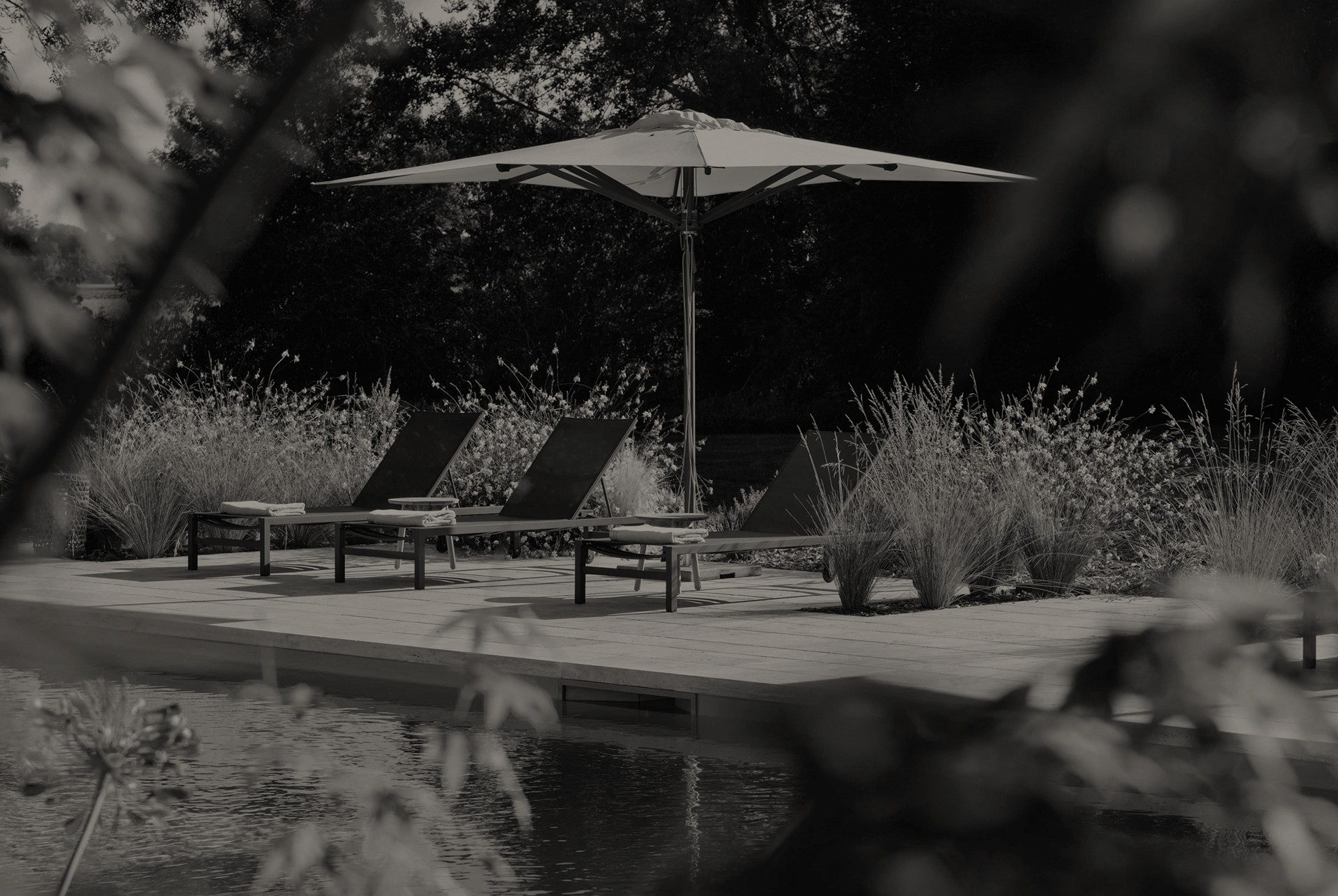 Terrasse extérieure moderne avec transats et parasol, entourée de végétation naturelle, représentant un espace d'aménagement paysager haut de gamme conçu par Invivo Paysage